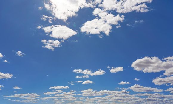 Bright sky background with few small clouds, strong sun shines through creating some lens flares.