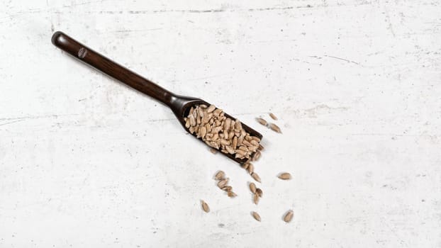 Peeled sunflower seeds in small wooden scoop, placed on white stone like board, view from above.