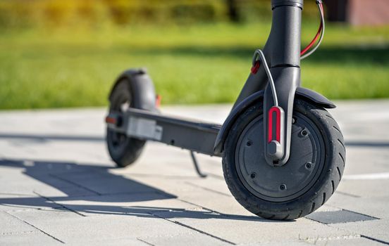 Electric scooter parked on tiled stone pavement - closeup detail on front wheel.