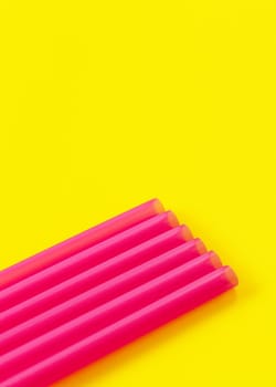 Six pink plastic drinking straws on yellow board, forming diagonal line - abstract closeup detail, space for text above.