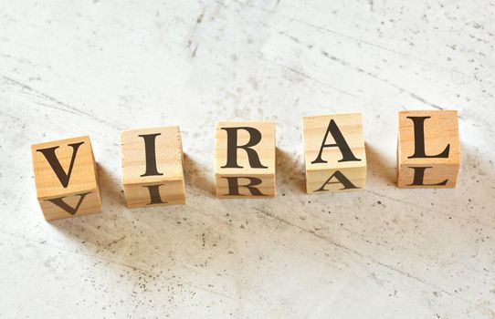 Five wooden cubes with word VIRAL on white stone like board, view from above.