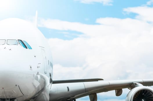 Close up of large white passenger plane with cockpit and wing in foreground. Blue sky with clouds in background. Travelling by air transport. Fast and comfortable trip by airplane.