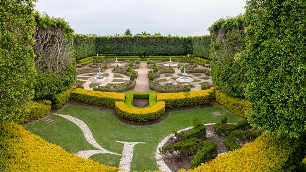 A decorative maze with plants and water fountains in a large garden