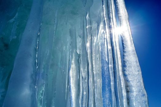 Long icicles made of ice against the blue sky and sun.