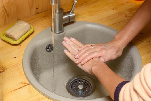 The girl's hands thoroughly wash their hands with soap in the kitchen sink