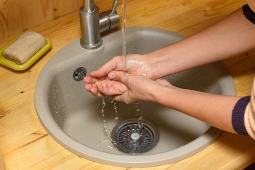 The girl's hands wash their hands in the sink set on a wooden tabletop
