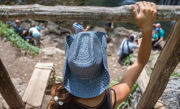 A young girl in a blue straw cowboy hat sits on a wooden bridge.