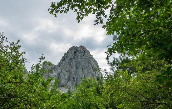 Inaccessible rocks surrounded by green forests and shrubs in hot summers in clear sunny weather.