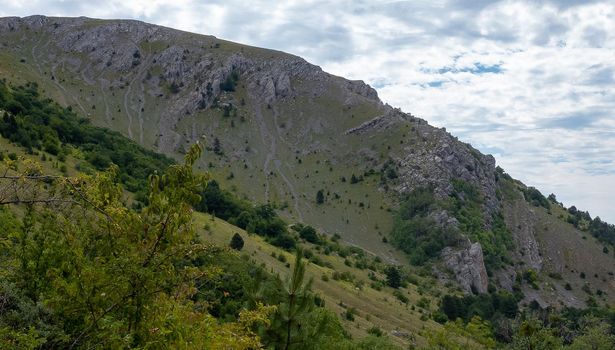 Inaccessible rocks surrounded by green forests and shrubs in hot summers in clear sunny weather.