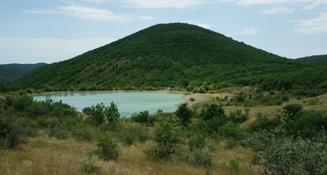 The shore of a mountain lake in the midst of inaccessible rocks, surrounded by a green forest.