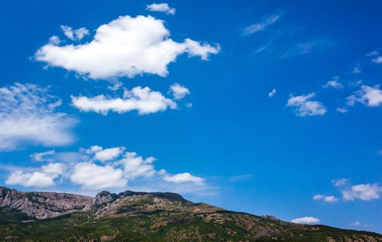 Inaccessible rocks surrounded by green forests and shrubs in hot summers in clear sunny weather.