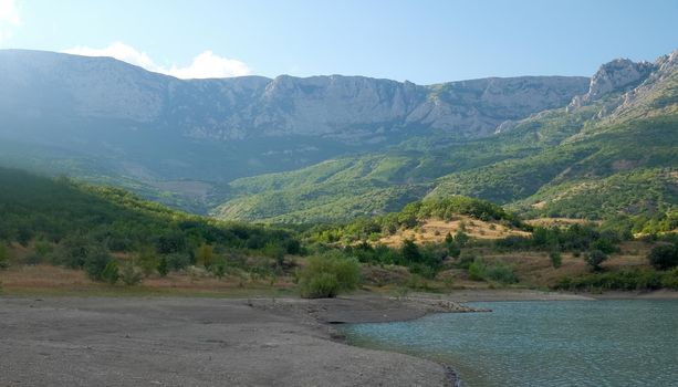 The shore of a mountain lake in the midst of inaccessible rocks, surrounded by a green forest.