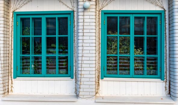 Two large turquoise windows on the veranda of a brick house.