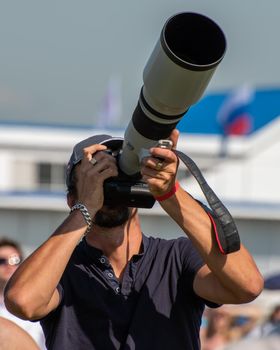 A man with a large professional camera and a telephoto lens photographs planes at an air show.