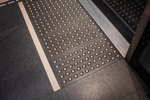 Close-up on indoor metal tactile paving for blind and visually impaired pedestrians. Platform edge at sliding doors on subway station in Brescia (Lombardy, Italy). Concept of accessibility for persons with disability.