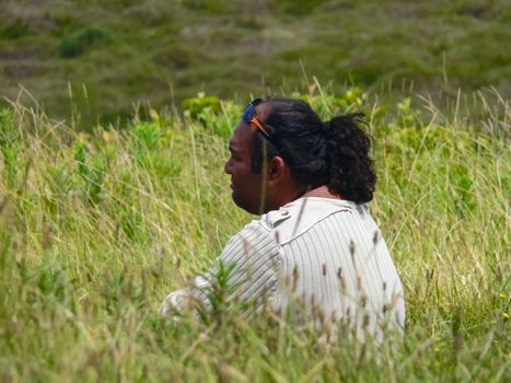 Angaroa, Easter Island, Chile - December 20, 2018: An indigenous resident of Easter Island sits in the grass.