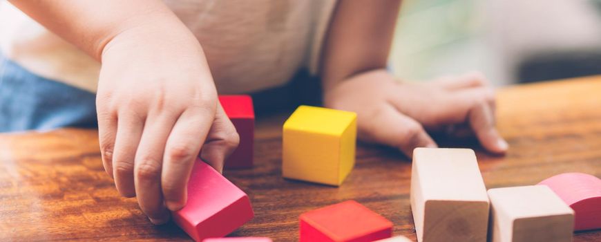 Closeup hand of boy playing wooden block toy on table for creative with enjoy, happy child learn skill for activity puzzle and creativity for game on desk at home, education concept, banner website.