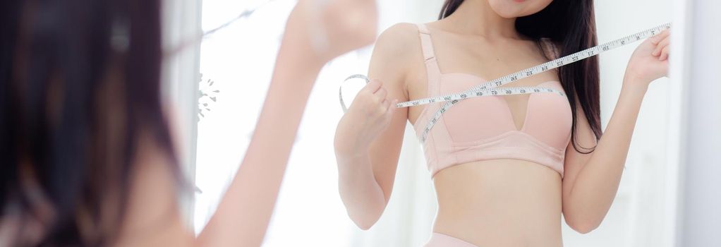Closeup young asian woman sexy body slim measuring breast for control weight loss looking mirror at room, asia girl figure thin measure size of bust for diet, health concept, banner website.