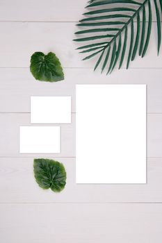 Blank paper sheet and name card mockup with copy space and leaf on wooden table, poster and invitation, postcard and business card decoration your design or branding, nobody, flat lay, top view.