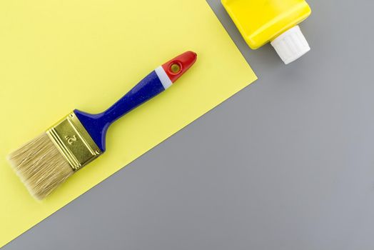 Renovation and color trends concept with clean paintbrush and pigment bottle on a two tone grey and yellow background with copy space viewed as a flat lay.
