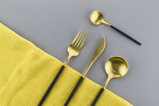 Set of stylish black and gold cutlery on a two tone grey and yellow background with copy space viewed as a flat lay. Main color trend of the year