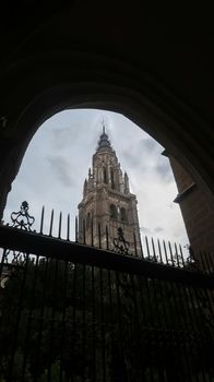 View of main tower of Cathedral of Toledo with backlit fence during a cloudy day