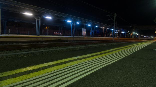 Line of hazard warning tactile paving along the edge of platform at the train station at night