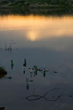 Glass bottles float in the pond. Debris in the water.