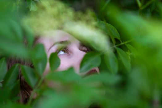 Young woman poses among the plants, watching and camouflaging.