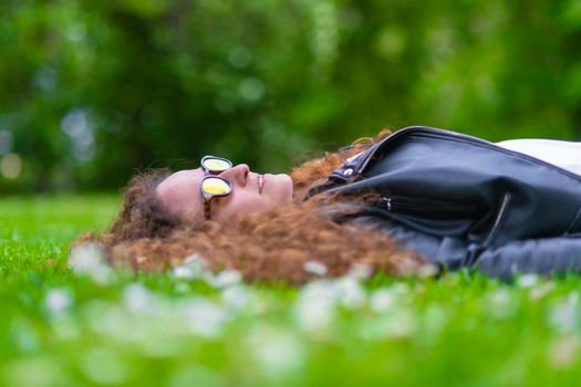 Woman lying relaxing on the grass looking at the sky with sunglasses, curly hair.