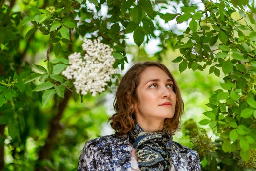 Young woman poses among the plants, looking at one of them.