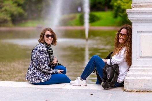 Talking sitting on a lake with fountain, they are mother and daughter.