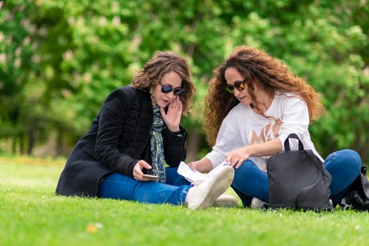 Talking and studying, with phone, relaxed in the park, sitting on the grass.