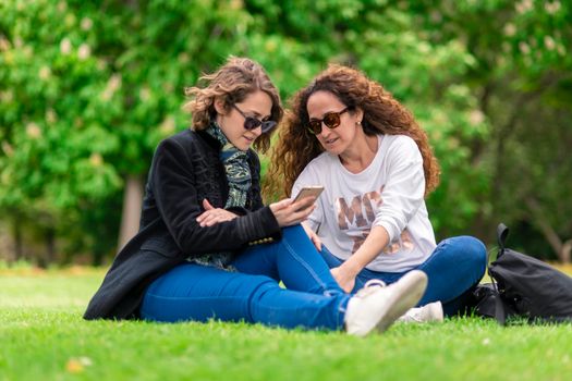 Talking and studying, with phone, relaxed in the park, sitting on the grass.