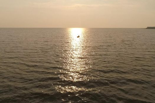 A fisherman in a boat in the sea against the sunset.