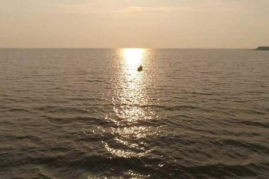 A fisherman in a boat in the sea against the sunset.