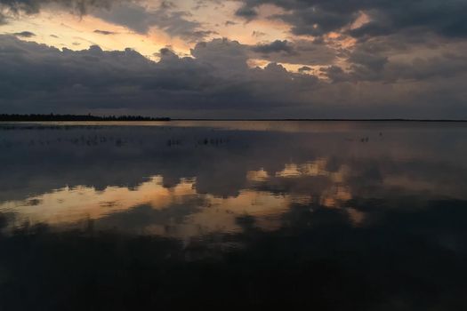 The sky is in zagon with clouds above the pond. Sunset time.