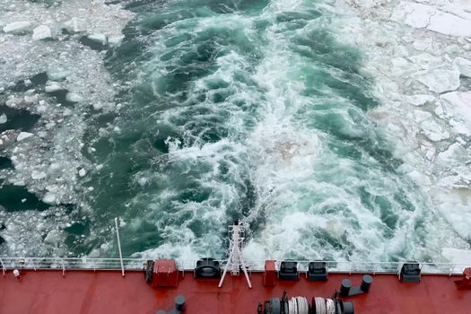 A trail on the water from the ship. Arctic and ice on the water. The propellers of the ship smeared the water.