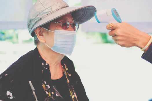 hand measuring body temperature of old woman with infrared forehead thermometer gun