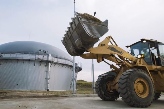 Tractor with a bucket against the background of the gas tank at the station.