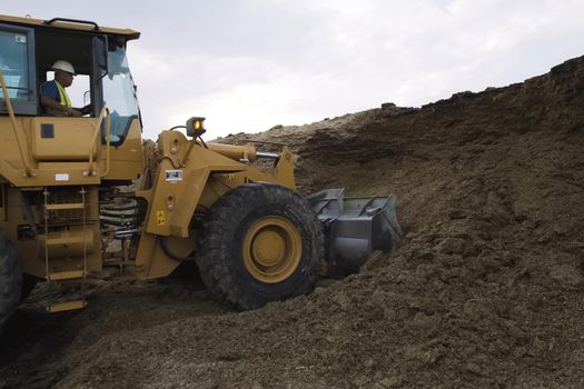 Novosibirsk, Russia - June 20, 2019: A tractor with a bucket flattens the soil. The greder flattens the ground.