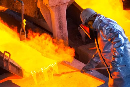 Worker at a steel mill. The worker mixes the molten metal.