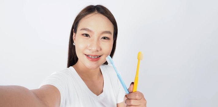 Asian teen facial with braces and toothbrush smiling to camera to show dental orthodonic teeth which include professional metal wire material from orthodontist. studio shot white background. Dental brace concept.