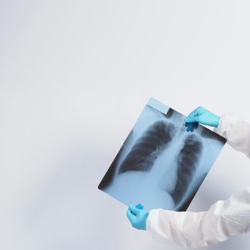 Xray film of Covid 19 lung damage and holding by doctor hand in medical glove and PPE or Personal Protection Equipment suit. Studio shot white background. Coronavirus pandemic and Healthcare medical concept.