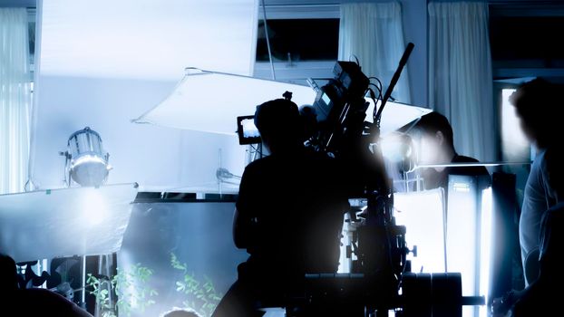 Silhouette images of video production behind the scenes or b-roll or making of TV commercial movies that film crew team lightman and videos cameraman working together with movie director in studio.