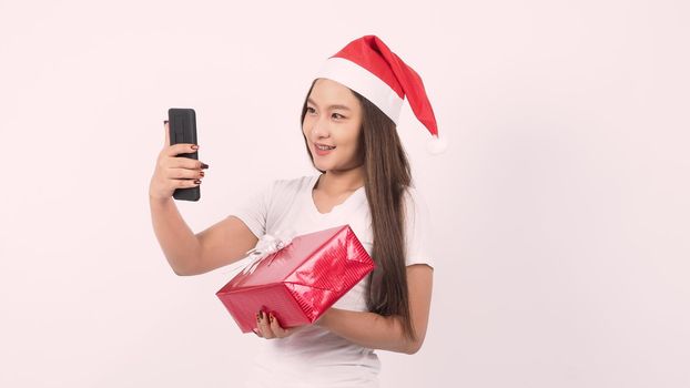 Girl hold gift box make selfie or video online with x-mas christmas prop decoration. Asian Thai teen woman taking online-selfie to celebrate festive season with her friend by red giftbox. studio shot.