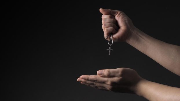 Cross or crucifix pendant and necklace in man hand on black color background in studio which represent praying for god or jesus and thank gods for giving peaceful and faithful to people. silver cross. religion belief concept.