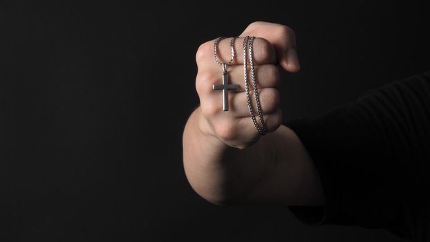 Cross or crucifix pendant and necklace in man hand on black color background in studio which represent praying for god or jesus and thank gods for giving peaceful and faithful to people. silver cross. religion belief concept.