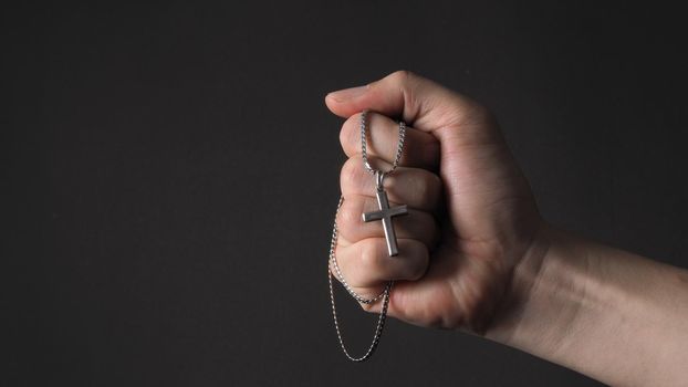 Cross or crucifix pendant and necklace in man hand on black color background in studio which represent praying for god or jesus and thank gods for giving peaceful and faithful to people. silver cross. religion belief concept.