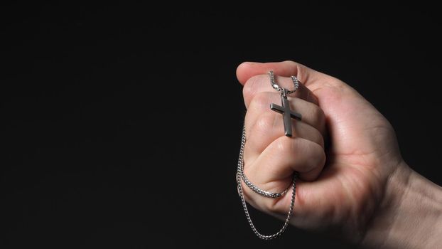 Cross or crucifix pendant and necklace in man hand on black color background in studio which represent praying for god or jesus and thank gods for giving peaceful and faithful to people. silver cross. religion belief concept.